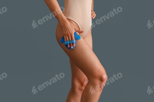 Preview: Woman in beige bodysuit massaging her thigh with palm shaped massage glove body massager