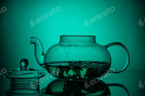 Preview: Glass transparent teapot with herbal tea and an open lid on a green gradient background