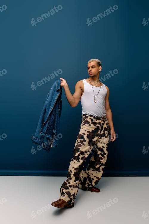 Preview: Stylish young man with dyed hair showcases denim jacket against blue backdrop