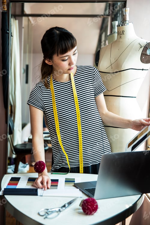 Preview: Japanese female fashion designer standing at desk, working in her studio.