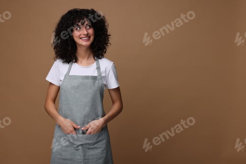 Preview: Happy woman wearing kitchen apron on brown background. Mockup for design