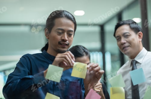 Preview: Asian business team meeting in the office using post it notes stick on glass wall