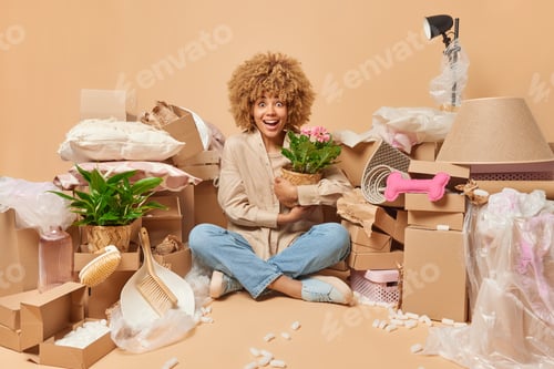 Preview: Photo of good looking woman sits crossed legs on floor with houseplant going to unpack things from c