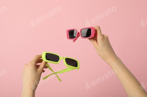 Preview: Pink and green sunglasses in female hands on pink background