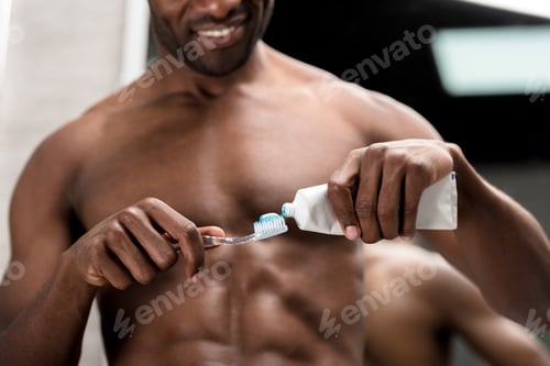 Preview: cropped shot of smiling african american man holding toothbrush and toothpaste
