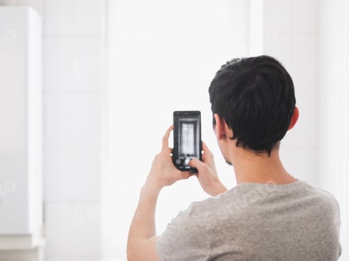 Preview: A young caucasian guy takes pictures on his smartphone of a small window in the bathroom