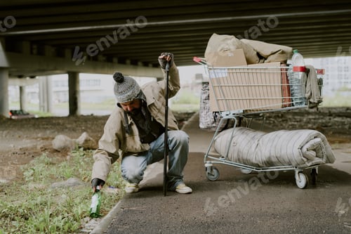 Preview: Homeless Caucasian Man Collecting Bottle Beside Shopping Cart Outdoors