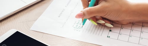 Preview: cropped view of woman holding green pen over planner with notes