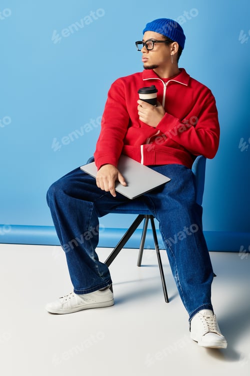 Preview: Chic young african american man with beanie and laptop sits casually on a chair