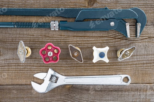 Preview: top view of plumber wrenches and various plumbing valves on rustic wooden tabletop