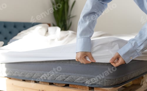 Preview: Woman putting cover on mattress indoors, closeup. Woman touching soft orthopedic mattress on bed at