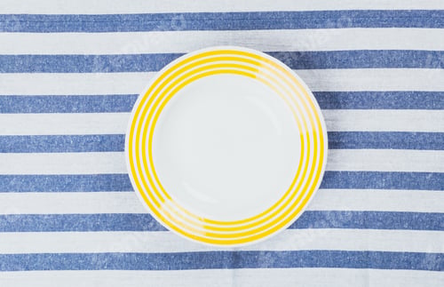 Preview: Vibrant plate with yellow stripes placed on a blue and white striped tablecloth