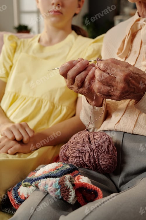 Preview: Senior Caucasian Woman Knitting Yarn Beside Teenage Girl Sitting Indoors