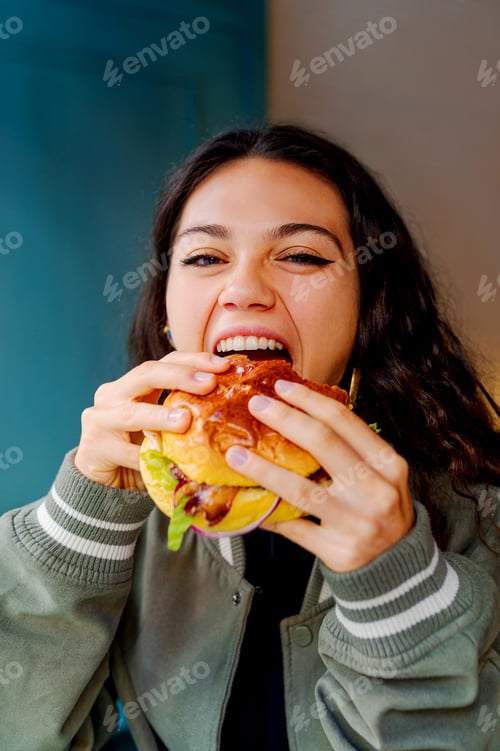 Preview: Happy young woman enjoying a delicious burger in a restaurant