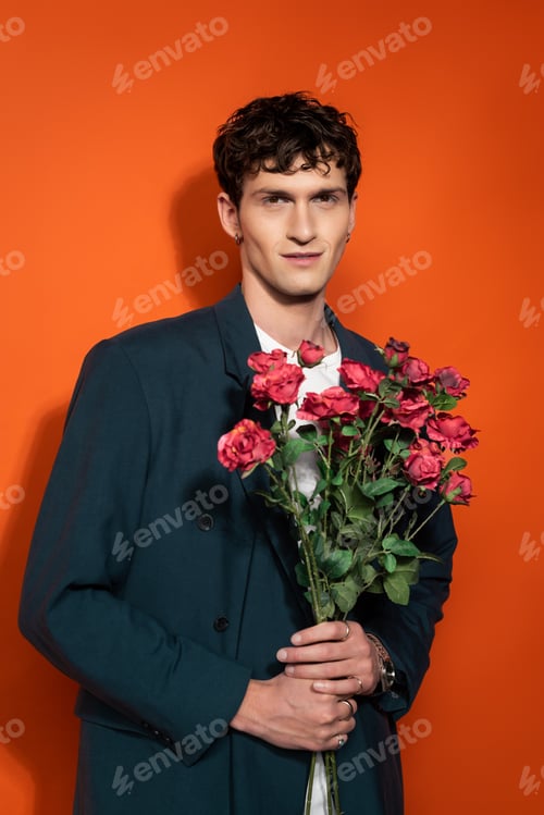 Preview: Portrait of smiling man in blue jacket holding roses on red background