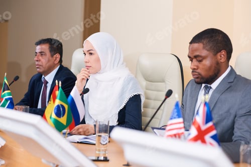 Preview: Pensive young female delegate in hijab listening to one of colleagues