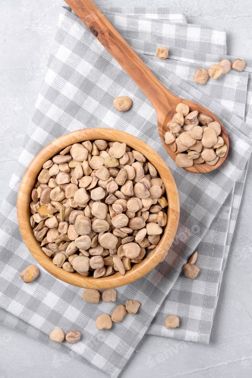Preview: Cicerchia or indian pea in a wooden bowl and spoon with napkin on grey table background