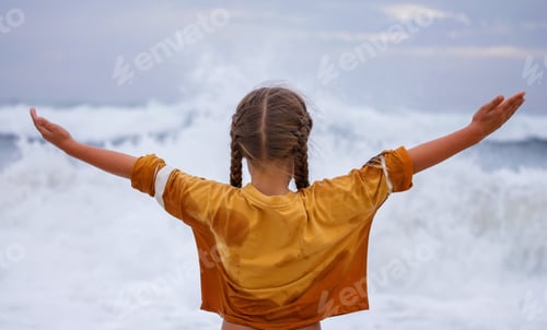 Preview: Girl stays on the ocean shore with arms open towards wind and waves. Storm in summer, courage