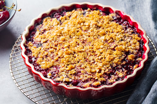Preview: Cherry, red berry crumble in baking dish. Grey stone background. Close up