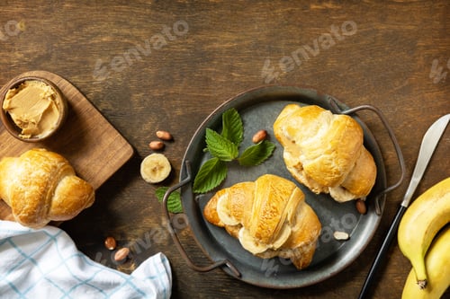 Preview: Tasty freshly baked croissants with peanut butter and banana on a rustic background.