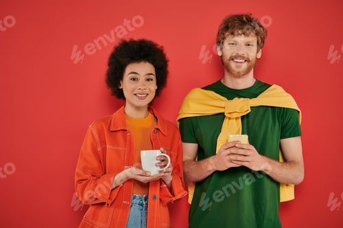Preview: multicultural couple holding cups of coffee on coral background, morning routine, cultural