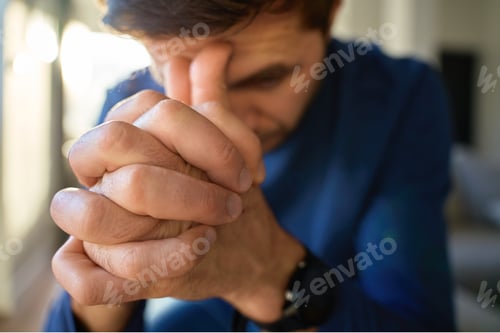 Preview: Nervous man sitting by window at home with clasped hands