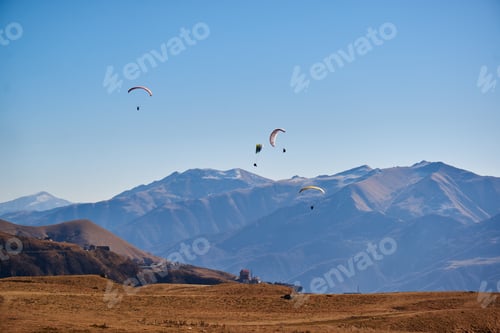 Preview: Paragliders soar gracefully in the clear sky next to the rugged brown mountain peaks.