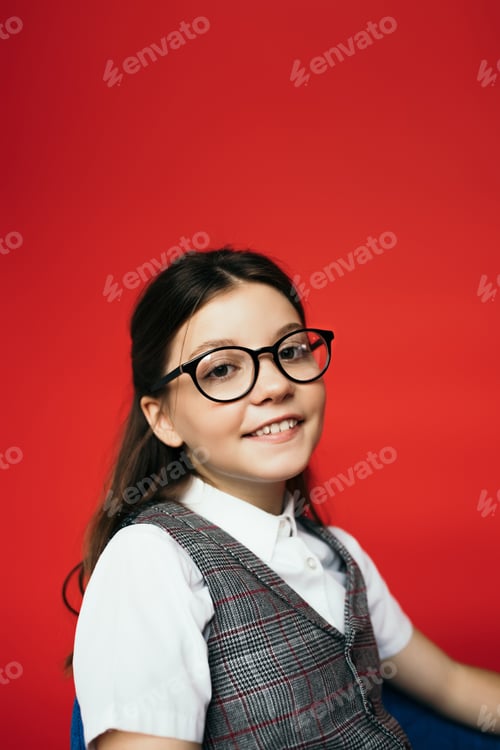 Preview: portrait of joyful brunette girl in eyeglasses smiling at camera isolated on red