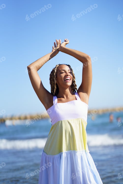 Preview: Black woman walking along the shore of the beach wearing a beautiful long dress.