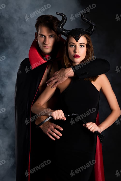 Preview: handsome man in cloak hugging girl with horns holding flogging whip on black with smoke
