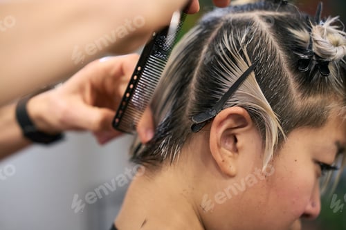 Preview: Hairdresser combing wet hair of young female model getting trendy haircut