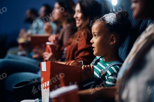Preview: black little girl eating popcorn during movie projection in cinema.