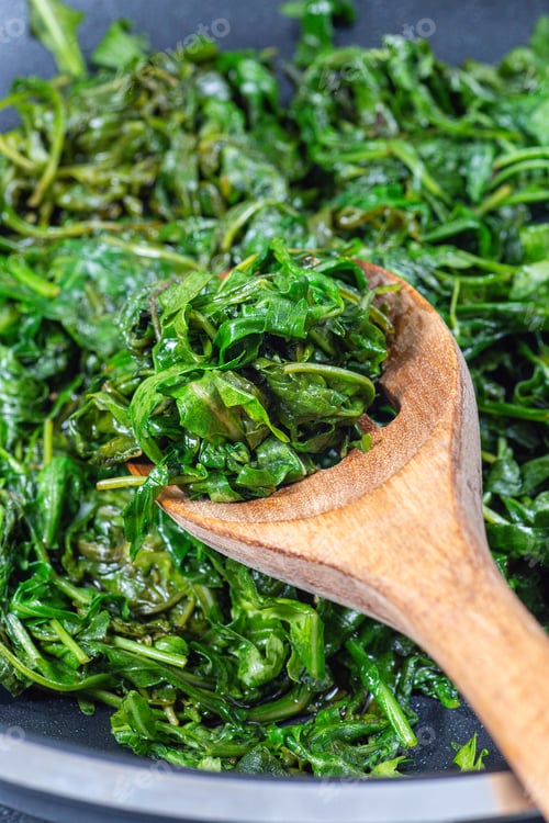 Preview: Wilted arugula or rocket salad, preparing a side dish in frying pan, vertical closeup
