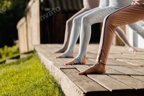 Preview: Four girls are practising yoga on a wooden podium in the garden in the open air