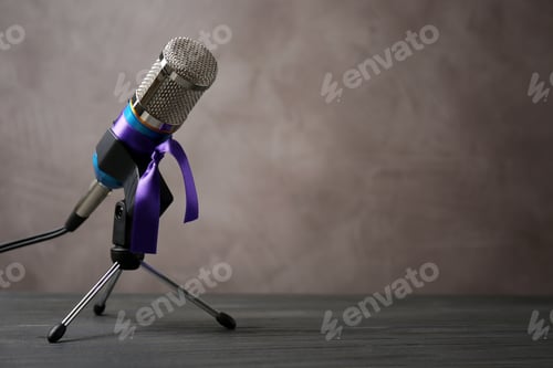 Preview: Microphone with purple awareness ribbon on table against brown background, space for text