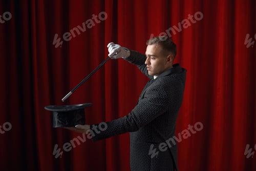 Preview: Young handsome illusionist performing magical trick with wand and hat