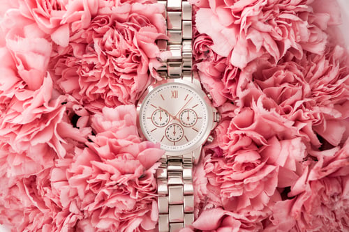 Preview: top view of elegant wristwatch lying on blooming flowers