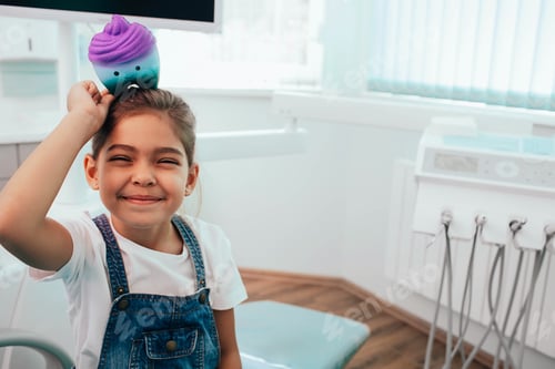 Preview: little mixed race girl visit dentist. He sitting at dental chair and holding toy tooth