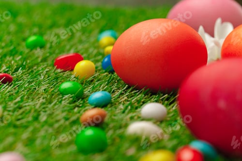 Preview: Close up photo of colored Easter eggs and candies on grass