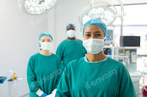 Preview: Portrait of smiling biracial female surgeon in mask and cap in operating theatre with colleagues