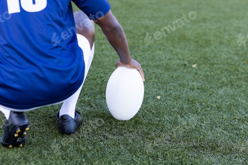 Preview: An African American young male athlete wearing a blue jersey is holding a rugby ball on a grass fiel