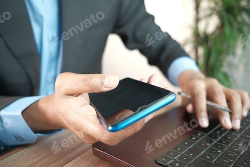Preview: businessman hand using smart phone and typing on laptop