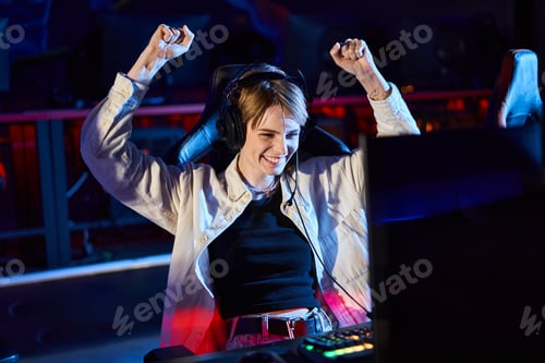 Preview: cheerful female gamer rejoicing and looking at monitor after winning game, cybersport concept