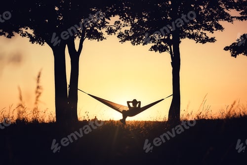 Preview: A girl's silhouette in a hammock between trees. A hammock in the background of the sunset.
