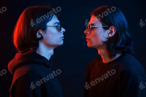 Preview: Creative photo. Portrait of twin brothers. Studio shot in dark studio with neon light