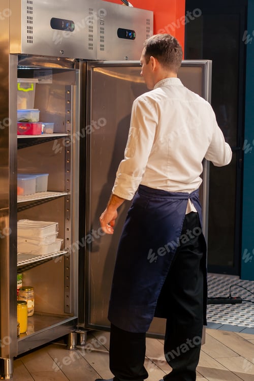 Preview: professional kitchen chef looks into the fridge and chooses ingredients for cooking food concept