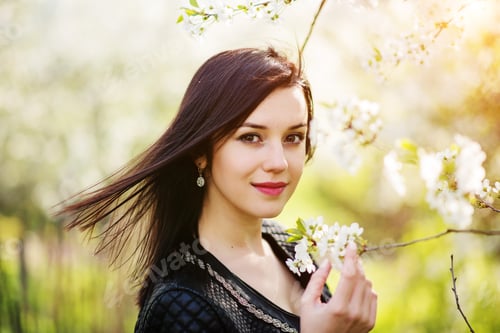 Preview: Close up portrait of young brunette girl with cherry blossom at spring garden.