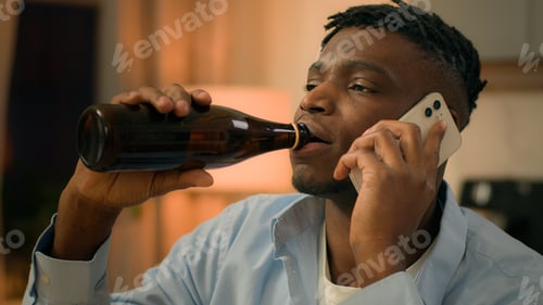Preview: Upset drunk African American depressed stress man drinking alcohol sad talking mobile phone problem