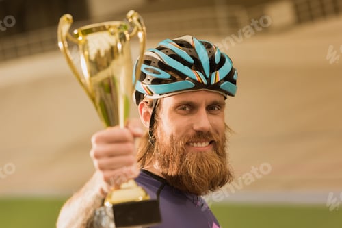 Preview: selective focus of smiling cyclist with champion cup looking at camera