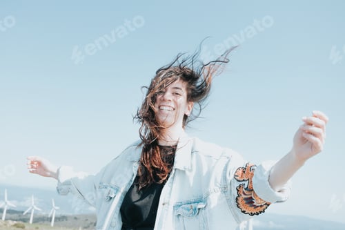 Preview: Young carefree woman on trendy modern clothes having fun, celebrating while the wind moves her hair.